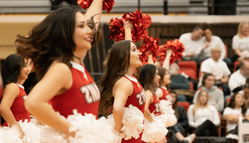 Saints cheerleaders in a line raise red pompoms in the air, white pompoms on their hips